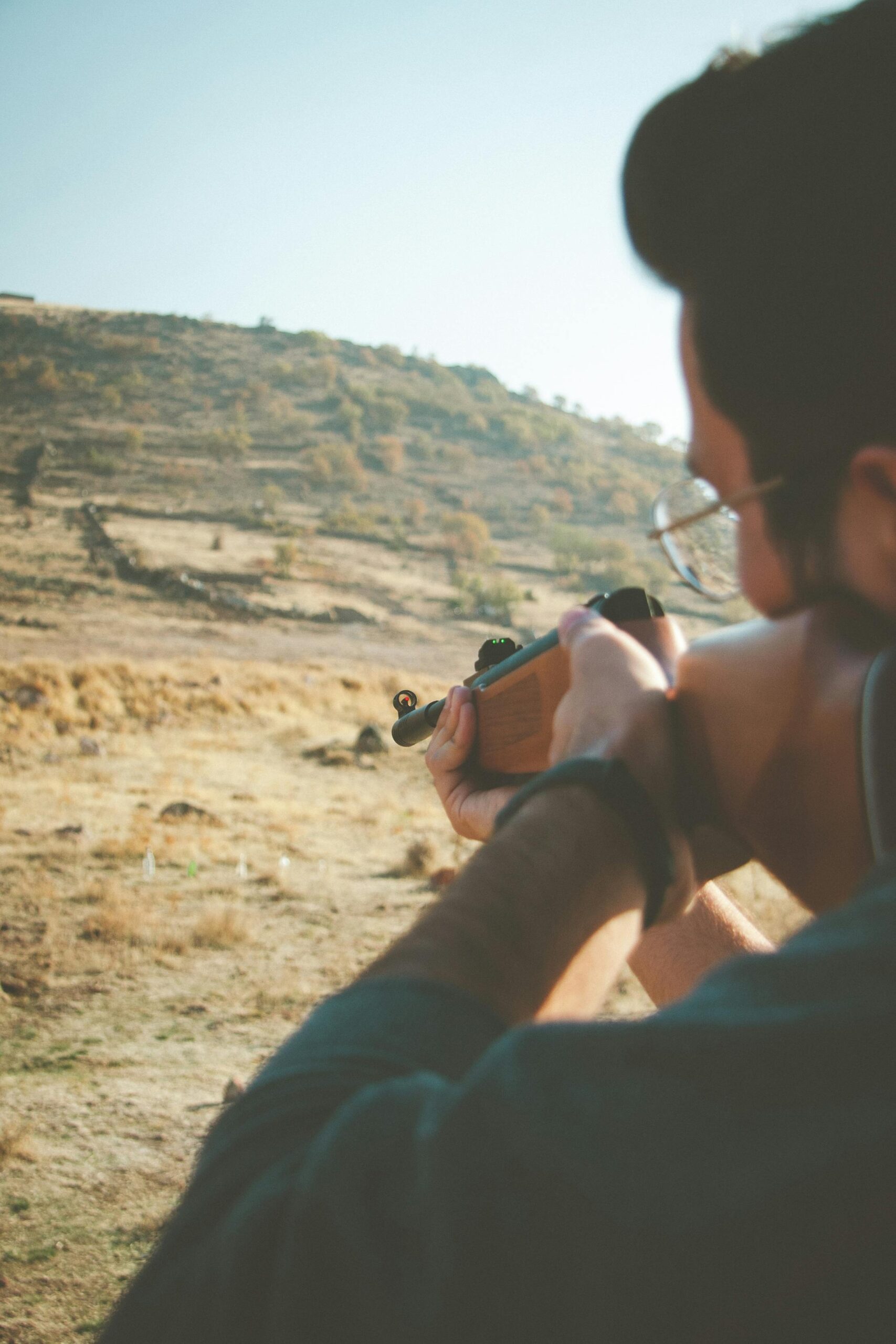 Person aiming a rifle in the desert landscape of Kayseri, Türkiye, on a sunny day.